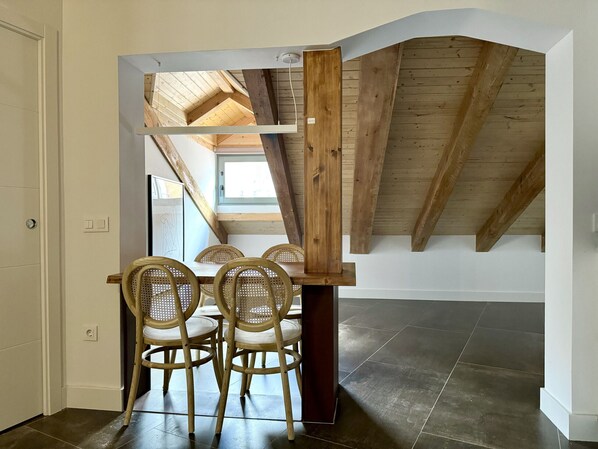 A dining area with a wooden table and four chairs, a slanted ceiling, and a view of the sky through a window. - CavaBajaSuites 401 PALACIO REAL (Madrid)