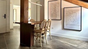 Un área de comedor con una mesa y sillas de madera, un techo alto con vigas a la vista y dos obras de arte enmarcadas en la pared.