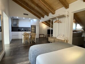 A modern loft-style bedroom with a large bed, a dining area with a table and chairs, a kitchenette, and a TV.