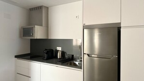 Moderni keittiö, jossa on valkoiset kaapit, ruostumattomasta teräksestä valmistettu jääkaappi, mikroaaltouuni ja kahvinkeitin.