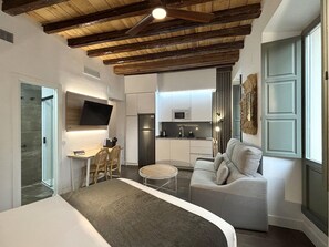 Ein modernes Schlafzimmer mit einem großen Bett, einer kleinen Essecke, einer Küchenzeile und einem Wohnbereich mit Sofa und Fernseher.