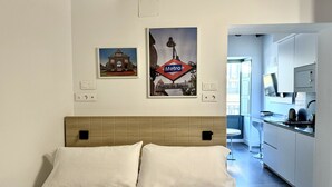 Una habitación de hotel moderna con una cama, kitchenette y dos obras de arte colgadas en la pared que representan monumentos.