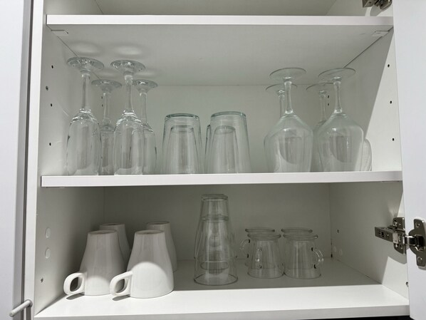 A white cabinet with shelves holding various glassware, including wine glasses and tumblers.