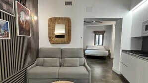 A modern interior with a grey sofa, a woven basket, a large mirror, and a bed in the background.