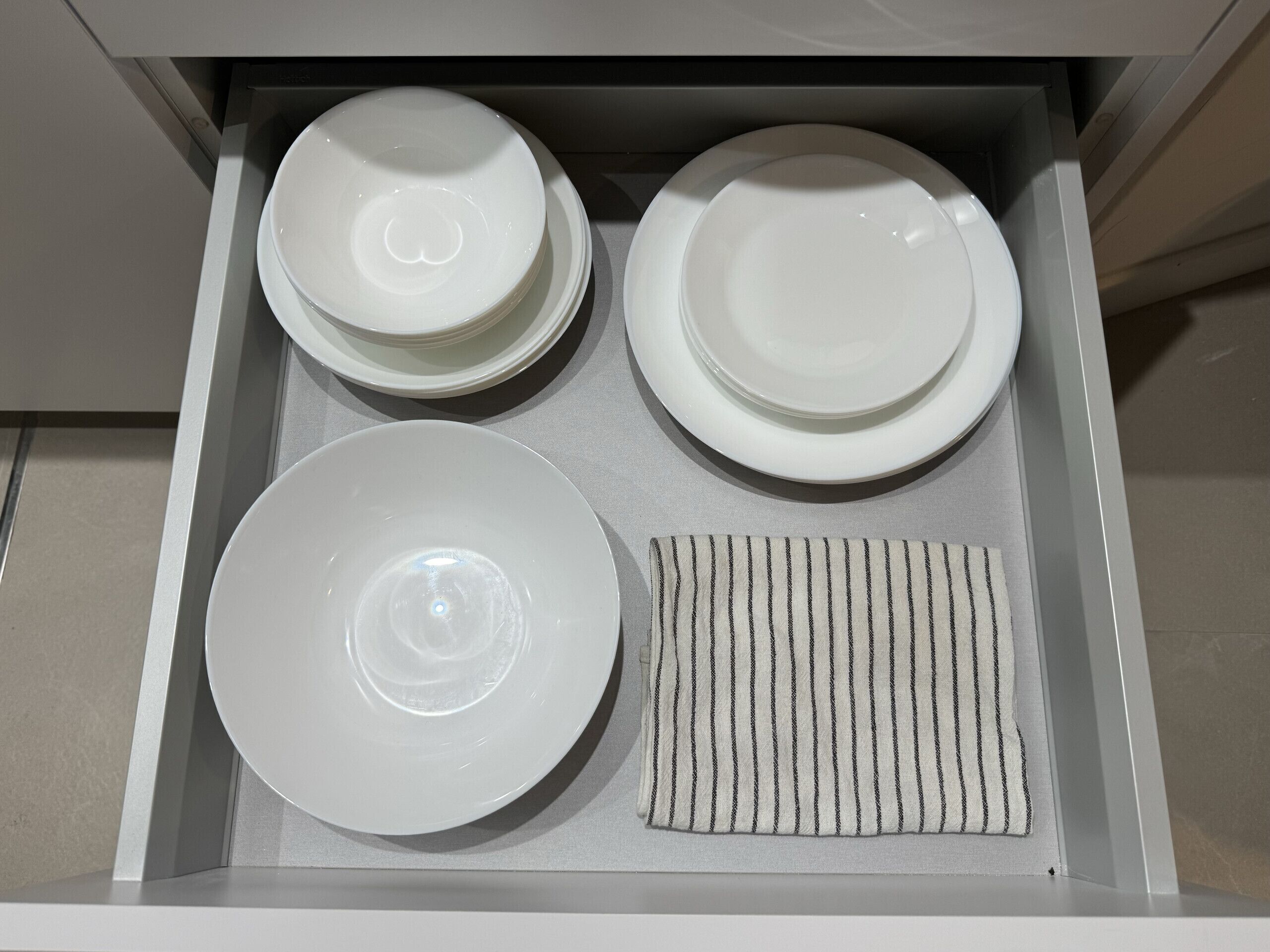 Un tiroir contenant des assiettes blanches, un bol blanc et un torchon à rayures.