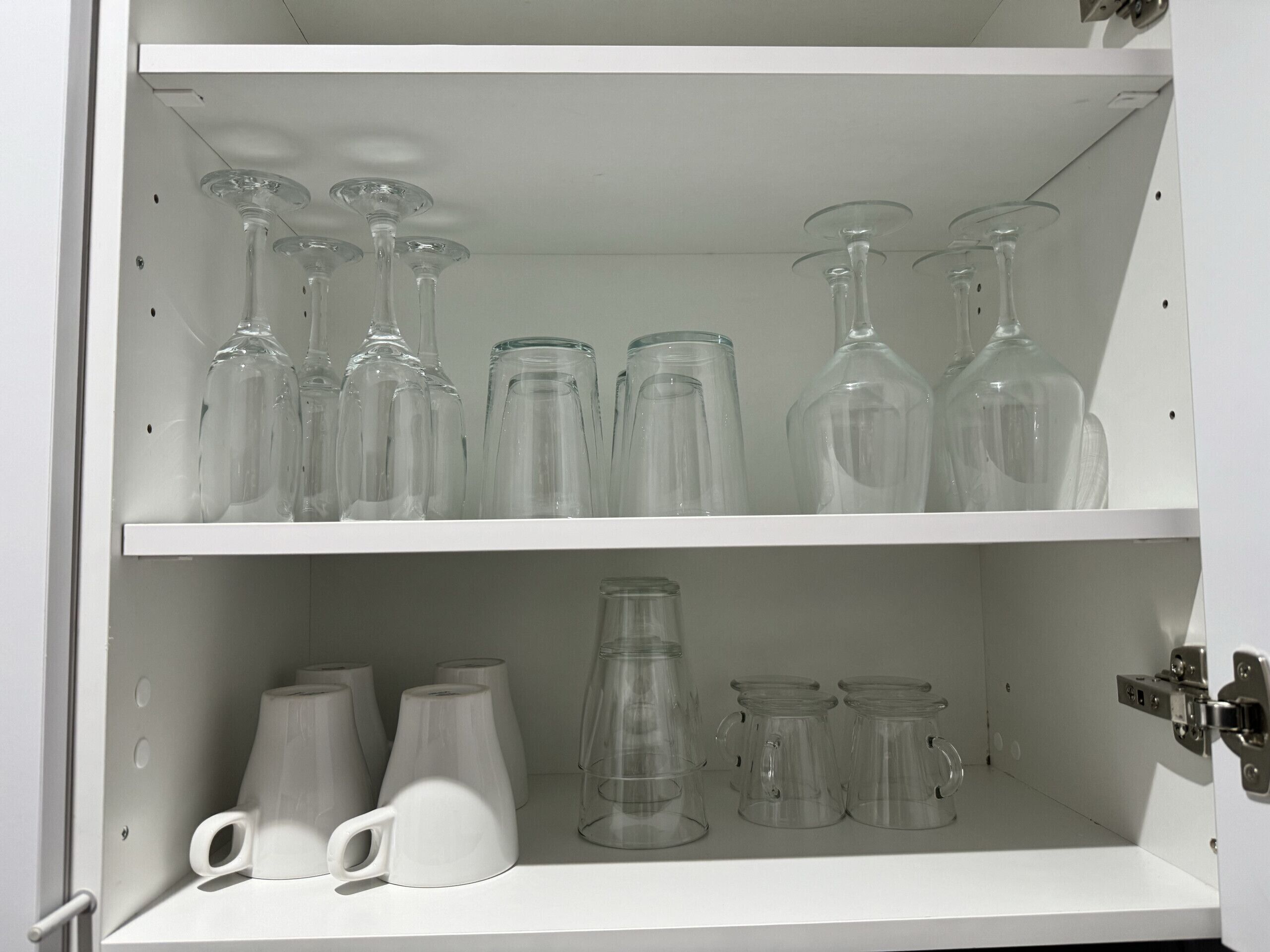 Un gabinete blanco con estantes que exhiben diferentes tipos de cristalería, como copas de vino y vasos.