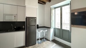 A compact kitchen with a built-in microwave, a stainless steel refrigerator, and a window with a view of the outside.