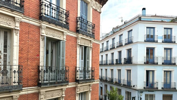 A multi-story building with red brick facades, blue shutters, and ornate iron balconies.