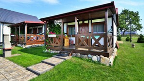 A two-story wooden house with a covered porch, stone steps, and a well-maintained lawn. - Cottage in Bobolin Near Baltic Beach (Darlowo)