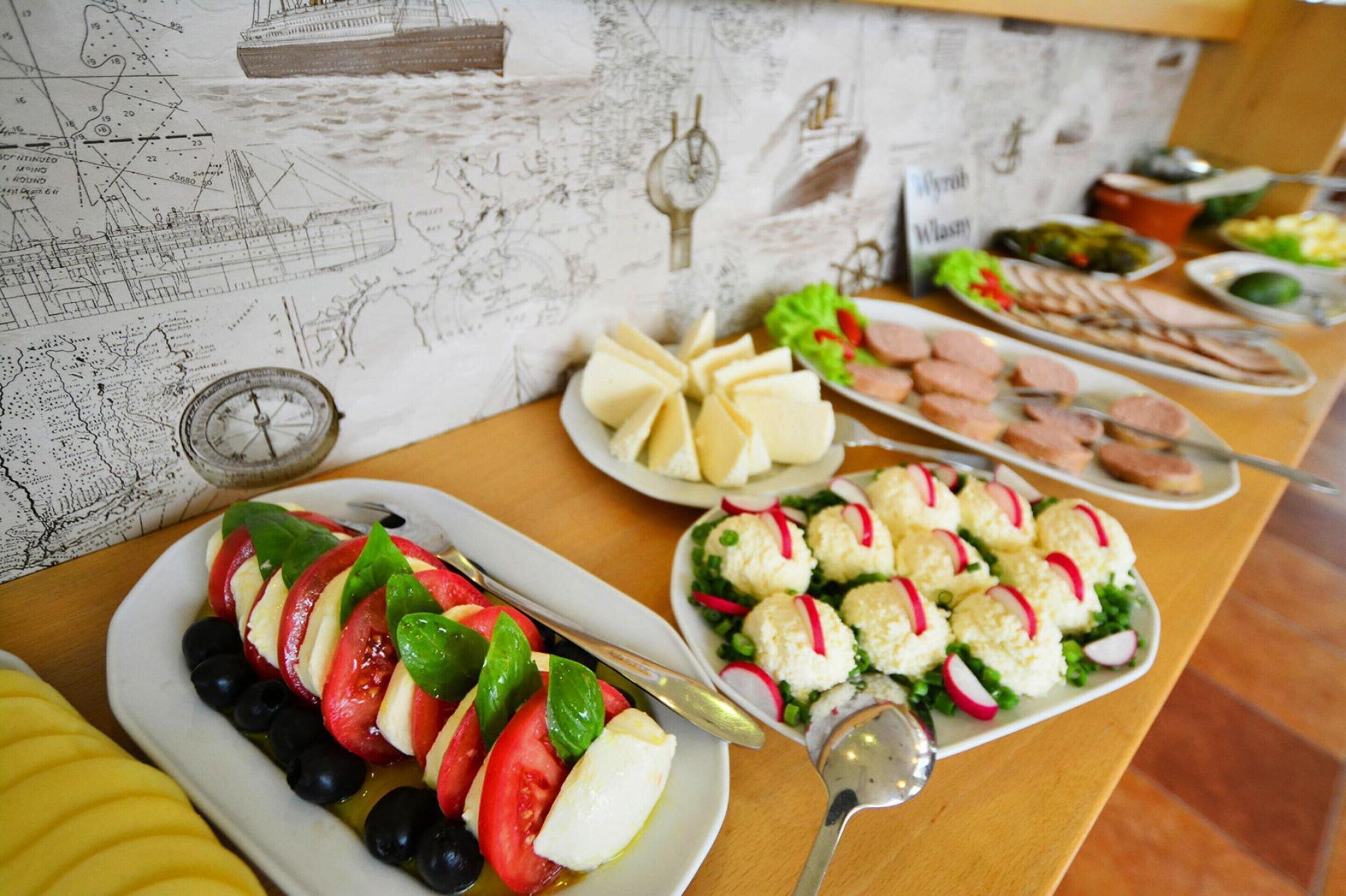 Ein reichhaltiges Buffet mit verschiedenen Speisen, darunter ein Tomate-Mozzarella-Salat, Käse und Fleisch.