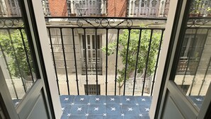 A balcony with a blue star-patterned floor, metal railings, and a view of a street with buildings and trees.