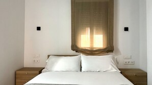 Ein Schlafzimmer mit einem Bett, zwei Nachttischen und einem Fenster mit durchsichtigen Vorhängen.