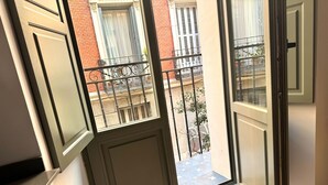 Ein Fenster mit Blick auf einen Balkon, ein Backsteinhaus und ein Metallgeländer.