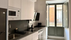 Eine moderne Küche mit weißen Schränken, einer eingebauten Mikrowelle, einer Kaffeemaschine und einem großen Fenster mit Blick auf ein Backsteingebäude.