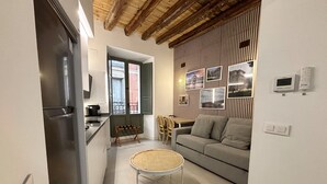 Un espacio habitable compacto con kitchenette, una zona de comedor y una sala de estar con sofá y mesa redonda.