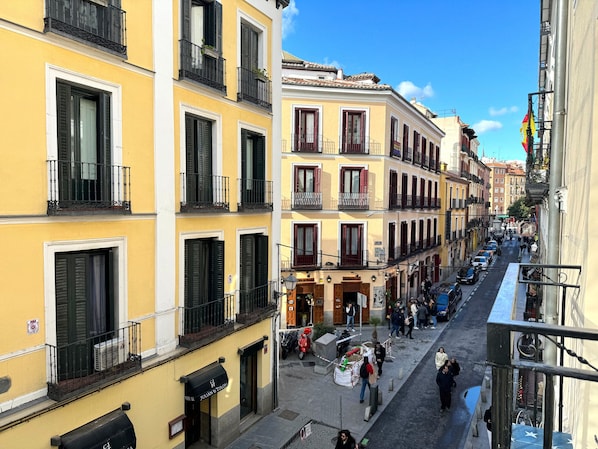 A narrow street lined with multi-story buildings, featuring balconies with metal railings and shutters.