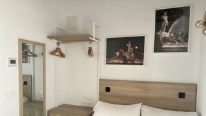 A bedroom with a wooden headboard, a bed with white linens, a bedside table, a mirror, and two framed pictures on the wall.