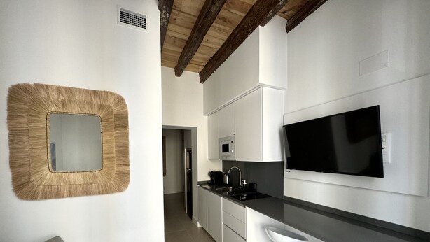 A modern kitchen with a large TV, white cabinets, and a unique wall mirror.
