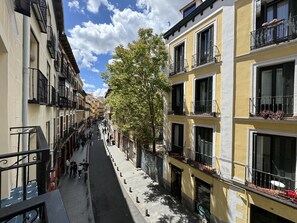 Una calle estrecha bordeada de edificios de varios pisos, con balcones y macetas llenas de flores.