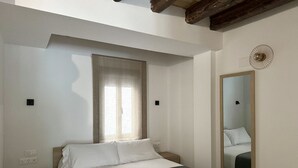 A bedroom with a bed, a bedside table, a mirror, and a window with curtains.