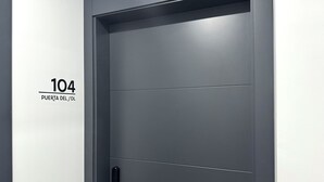 Una puerta moderna con cerradura de teclado numérico y manija, identificada con el número 104 y el texto 'PUERTA DEL SOL'.