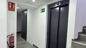 Un pasillo con un extintor en la pared, un letrero de salida de emergencia verde y una puerta con placa numérica.
