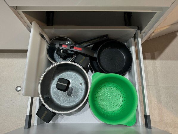 Un cajón de cocina con una sartén, una olla, un colador y una espátula.
