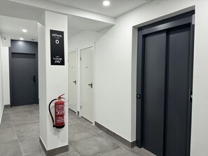 A hallway with a fire extinguisher mounted on a pillar, a sign indicating 'Planta Floor 0', and a door labeled 'Cava Baja Suites'.