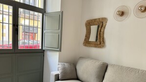 A living room with a grey sofa, a window with a view of a red car, and two wall-mounted mirrors. - CavaBajaSuites 004 EL RASTRO (Madrid)