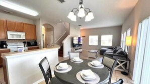Una cocina moderna con una isla central, comedor con sillas y sala de estar con sofá y televisor.
