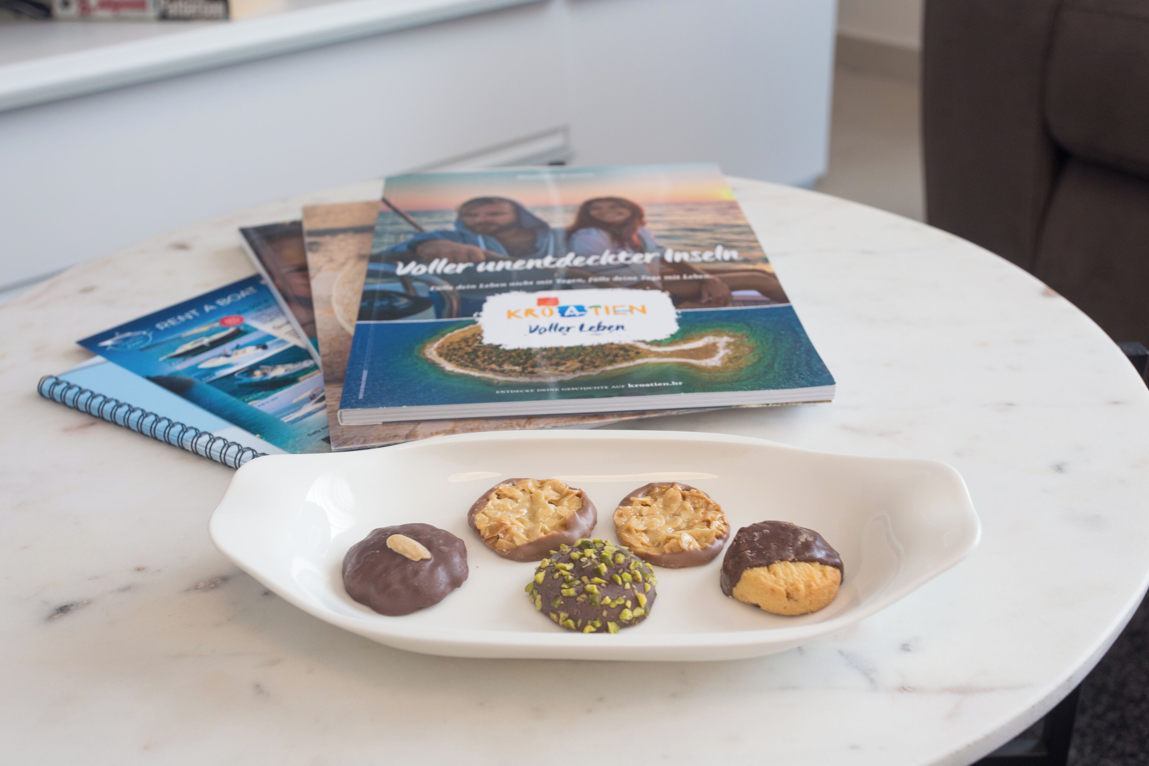 A white plate with five cookies on a marble table, surrounded by books and a notebook.