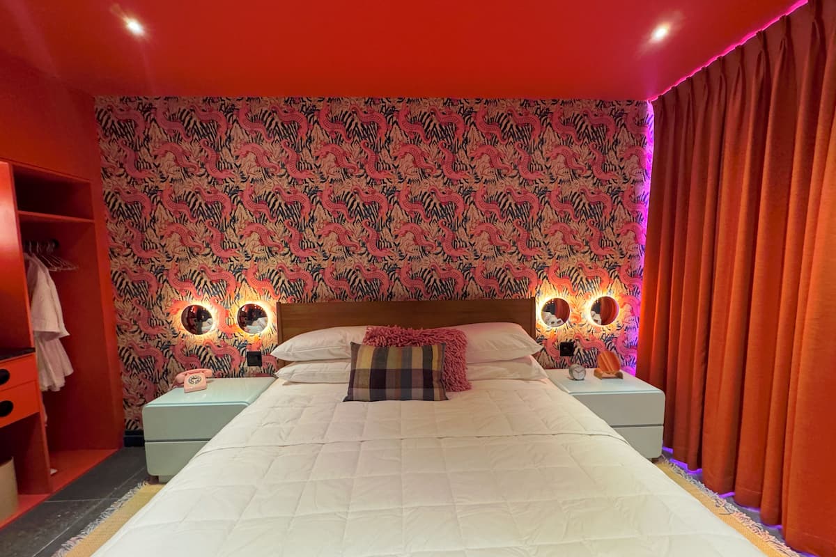 Une chambre à coucher avec un grand lit, deux tables de chevet avec des lampes, une armoire et un papier peint à motifs.
