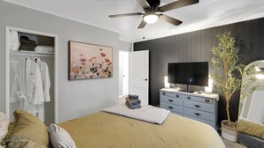 Ein Schlafzimmer mit einem Bett, einem Schminktisch, einem Fernseher, einem Deckenventilator, einem Gemälde und einem Kleiderschrank.