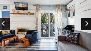 Una sala de estar con televisor, sofá, sillones, chimenea y balcón con mobiliario exterior.