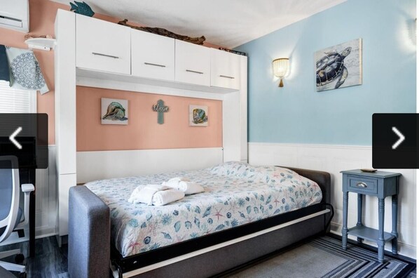 Un dormitorio con cama, escritorio y silla. Hay decoraciones en la pared y una lámpara.