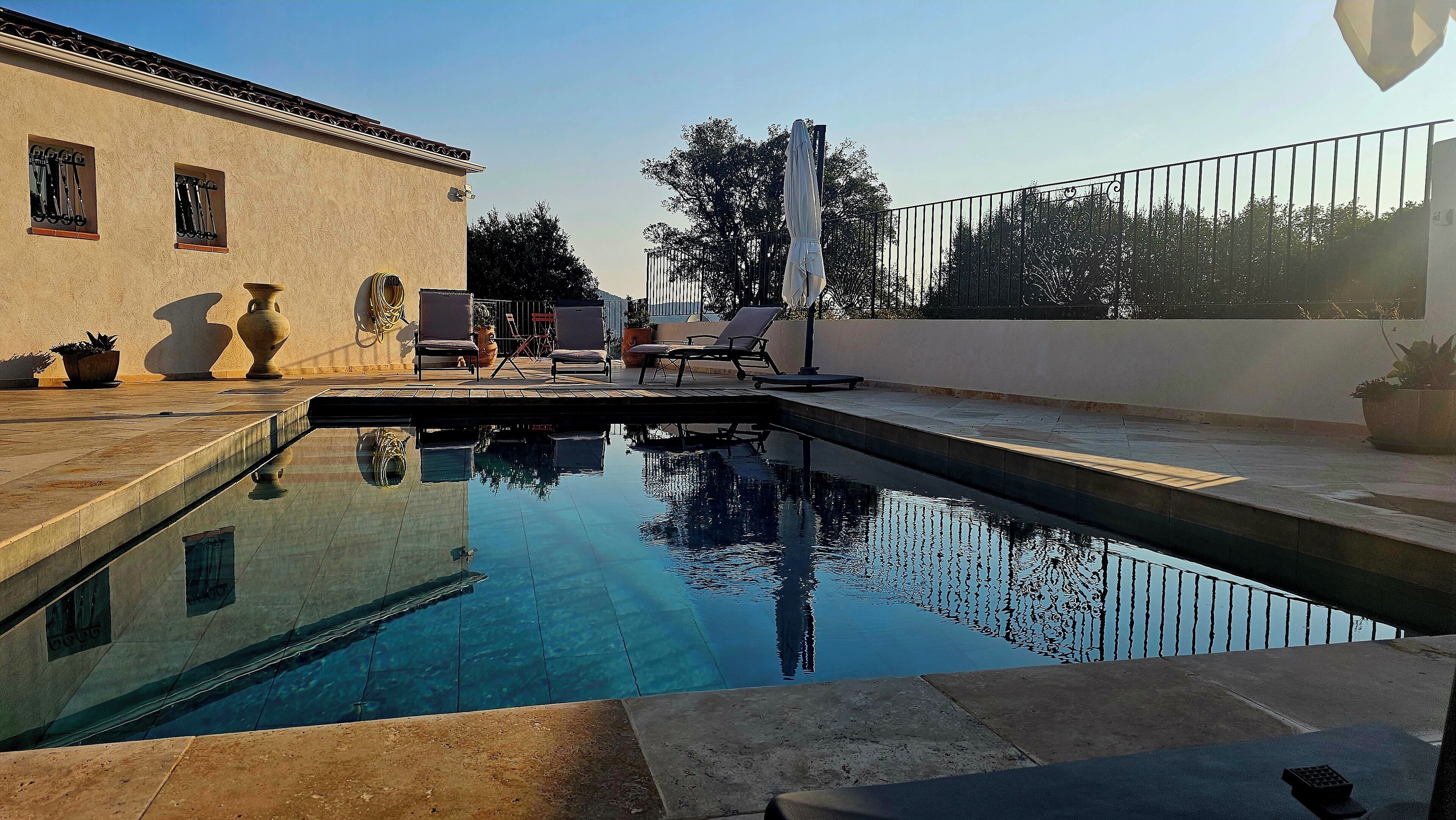 A swimming pool with clear water, surrounded by lounge chairs and potted plants.