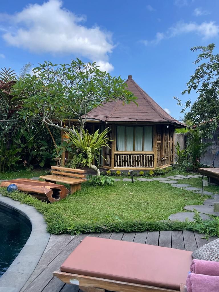 A small wooden house with a tiled roof, surrounded by a well-maintained garden and a wooden deck.