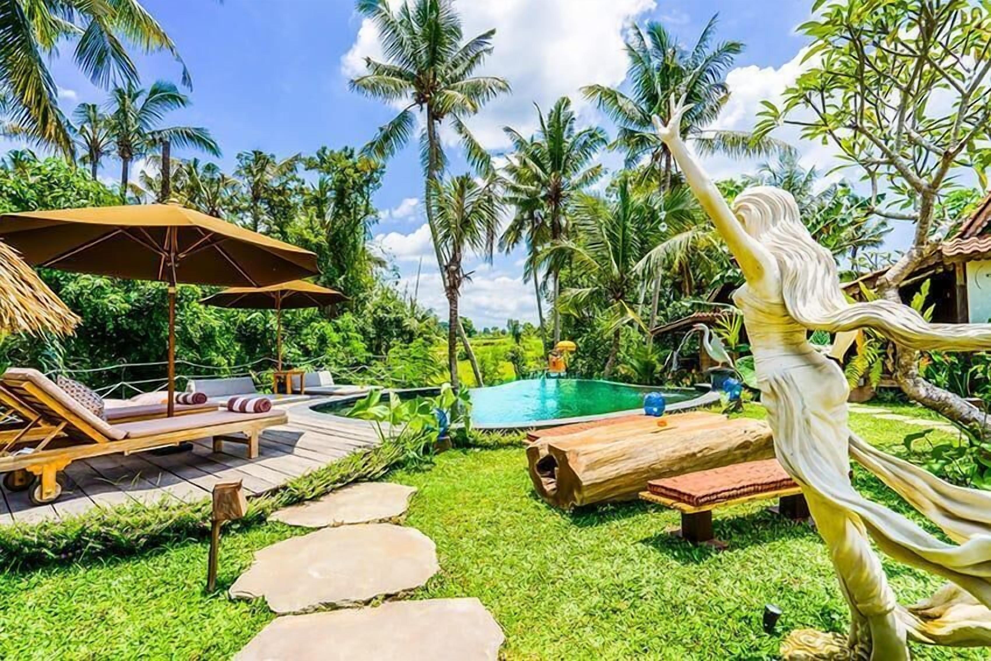 Uma área à beira da piscina com espreguiçadeiras, um banco de madeira e uma estátua.
