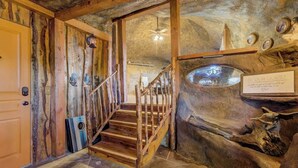 A rustic interior with a wooden staircase, stone flooring, and a 'Be Our Guest' sign. - Cave Cabin | Hot Tub, Fire Pit & Lake (Florissant)