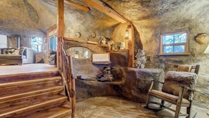A rustic interior with a stone wall, wooden staircase, and a rocking chair. - Cave Cabin | Hot Tub, Fire Pit & Lake (Florissant)