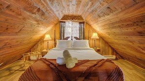 A cozy attic bedroom with a large bed, two bedside tables, and a window with curtains. - Cave Cabin | Hot Tub, Fire Pit & Lake (Florissant)