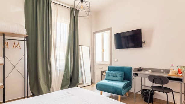 A hotel room with a bed, a desk with a chair, a television, and a window with curtains. - A Pisa con Amore (Pisa)