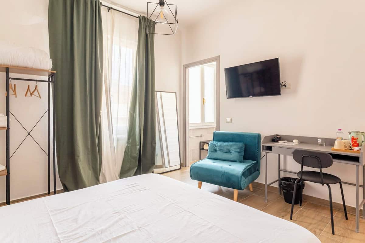 Una habitación de hotel con cama, escritorio con silla, televisor y ventana con cortinas.