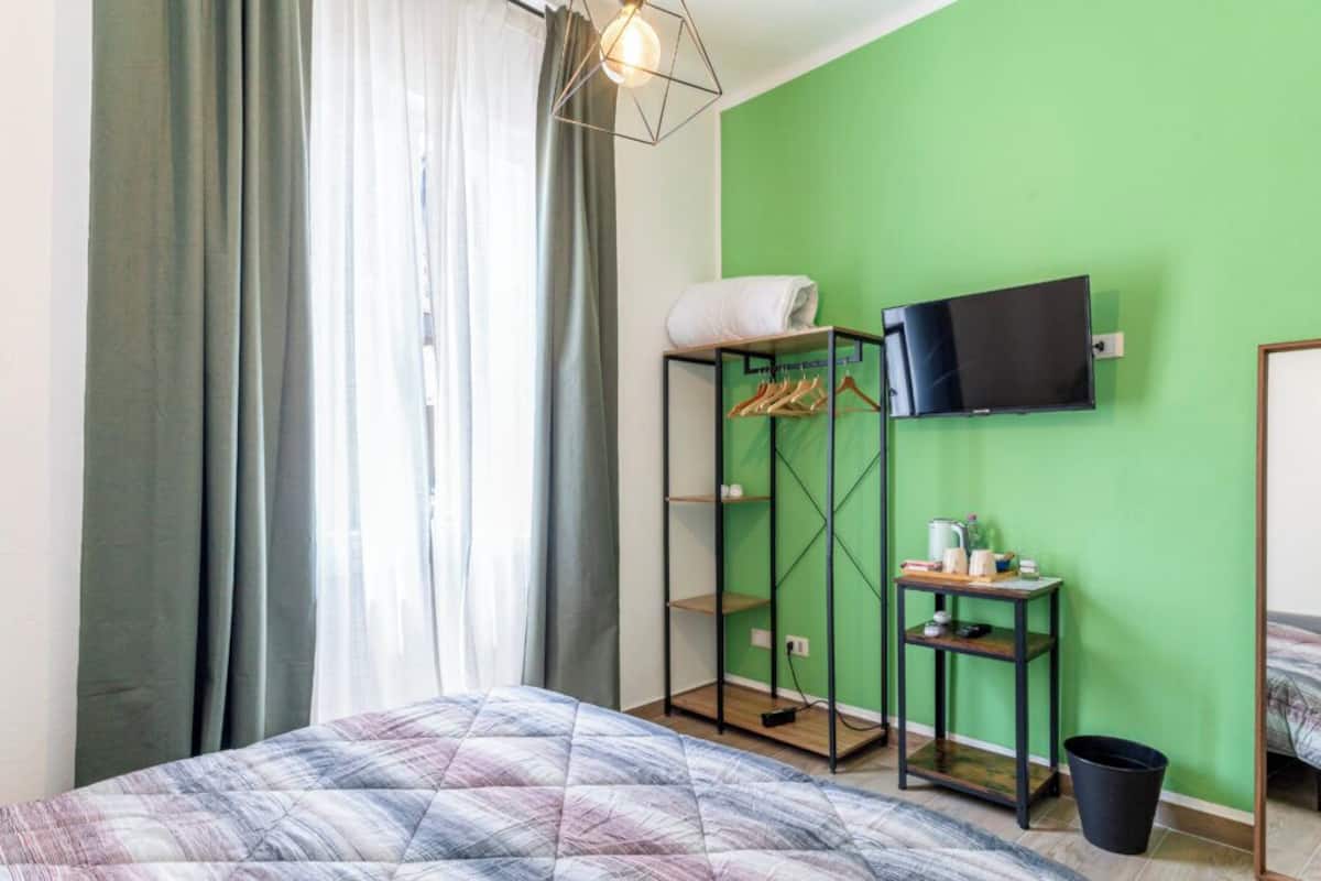 Una habitación de hotel con cama, armario, televisor y una pequeña mesa con objetos encima.