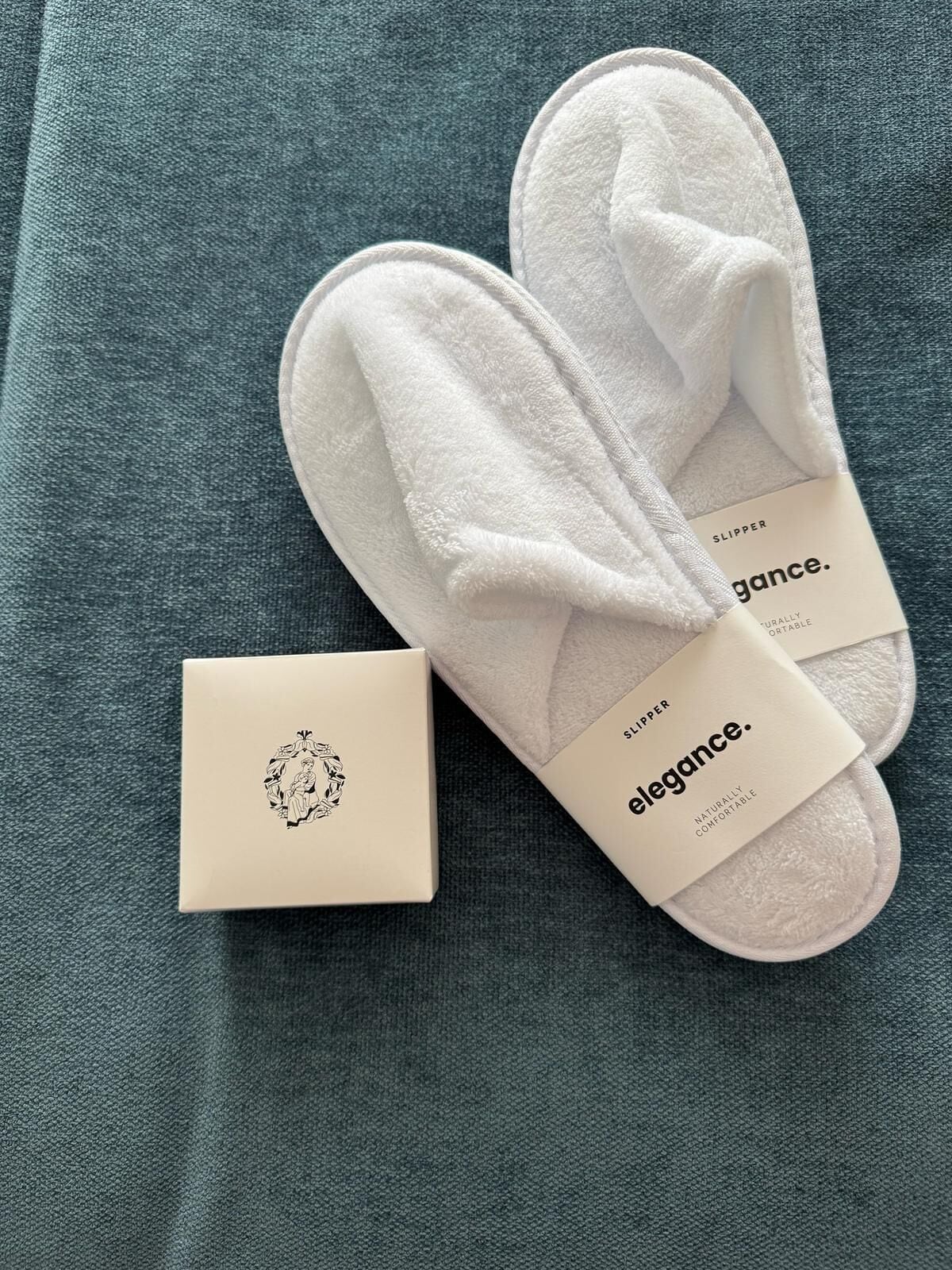 A pair of white slippers with a tag labeled "elegance." and a small box with a decorative design.