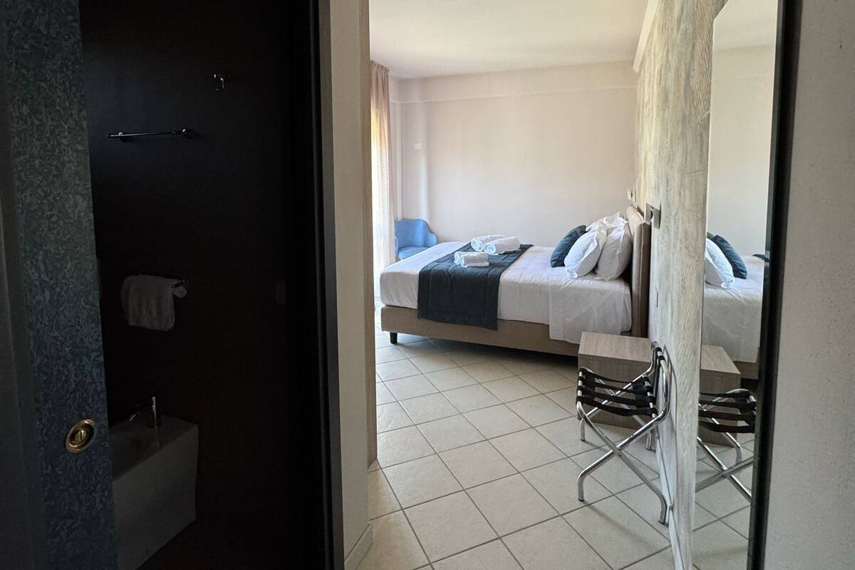 Una habitación de hotel con baño, una cama con almohadas, una silla y una pequeña mesa.