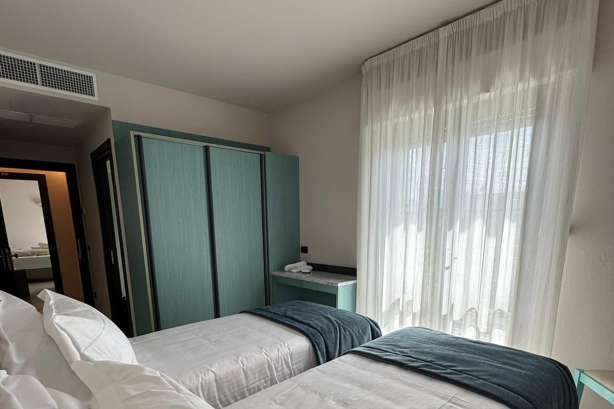 Habitación de hotel con dos camas, un armario, un escritorio y una ventana con cortinas.