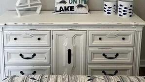 A room with a white dresser, two fish wall art, a pillow with 'HOOKED ON THE LAKE' text, and two mugs with fish designs. - Riverside 3BR Retreat | Tranquil & Family-Friendly (Indian River)