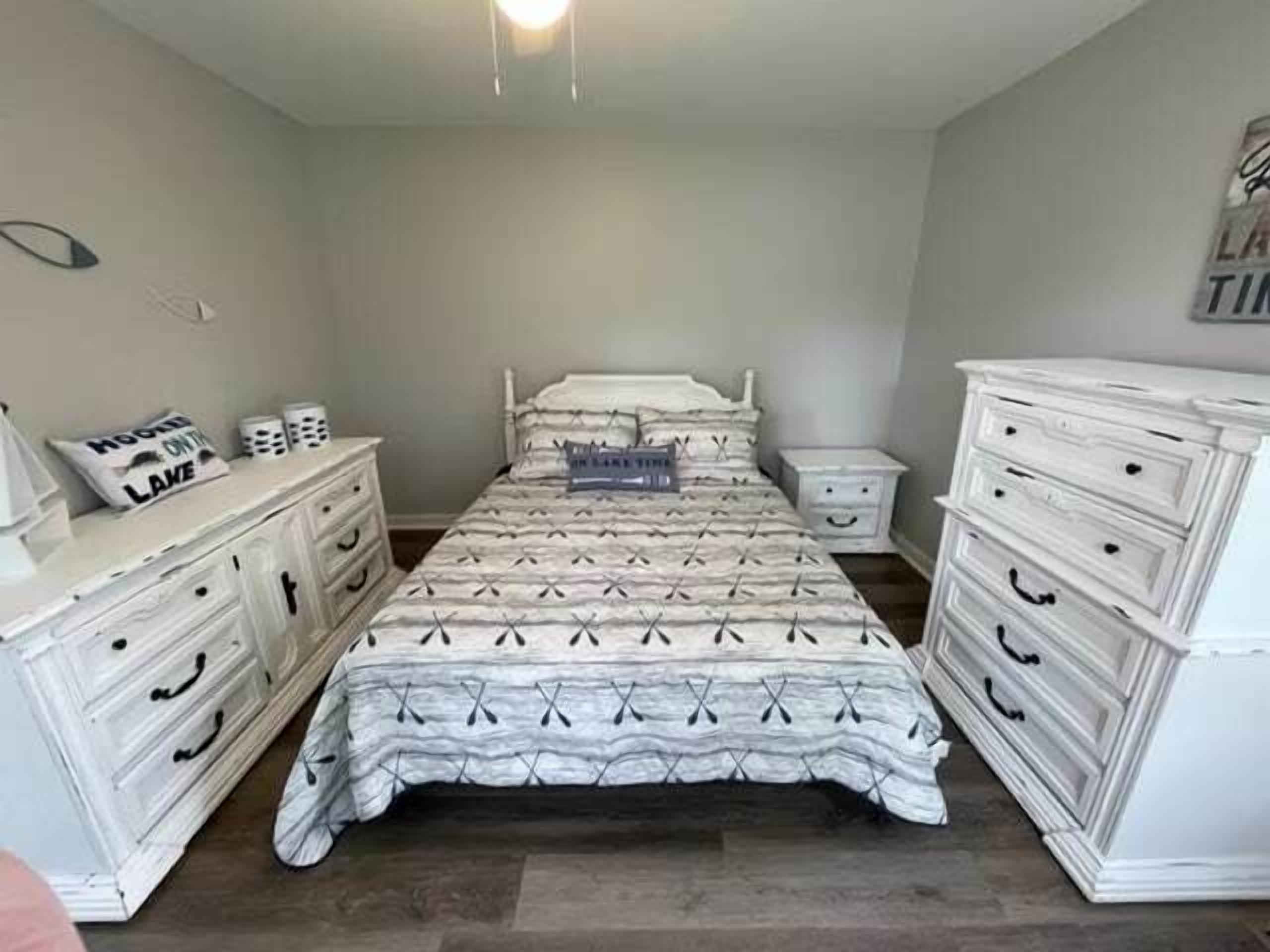 A bedroom with a bed, two nightstands, a dresser, and a wall with a sign.