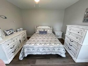 A bedroom with a bed, two nightstands, a dresser, and a wall with a sign.